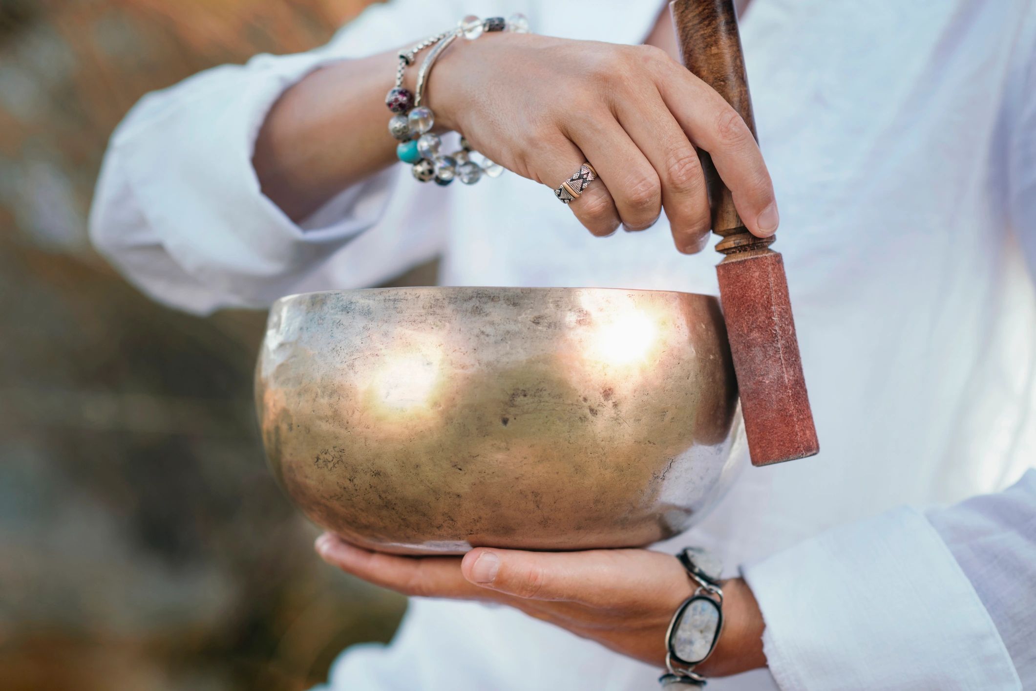 A woman in a white shirt holds a healing Tibetan singing bowl in her hand. The other hand is rubbing along the edge of the bowl. 