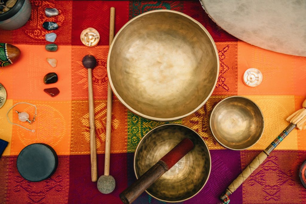 On a colorful cloth sits three healing Tibetan singing bowls. Lying next to them are mallets, strikers, and crystals. 