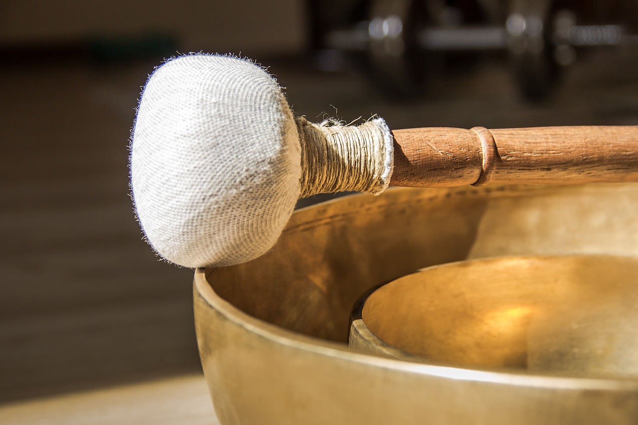 Two healing Tibetan bowls sit nested inside one another. On top of the bowl, is a cloth mallet with a wooden handle.