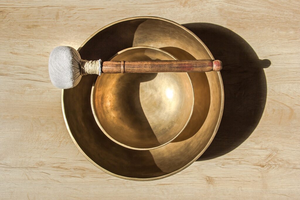 Two Tibetan bowls are sitting on a table, one inside of the other. On top of the bowls is a mallet. 