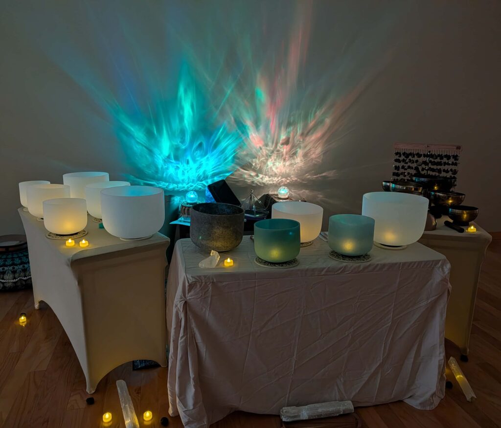 A sound bath set up with tables, crystal singing bowls, lights, crystals, and candles.