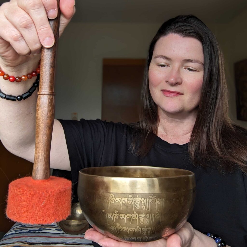 Lara Dunning at Sound Healing Therapy with Lara strikes a Tibetan healing bowl with a mallet.