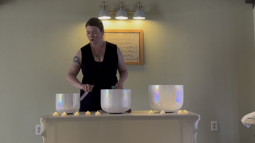 Sound healing practitioner Lara Dunning playing crystal bowls at a vocal toning event.