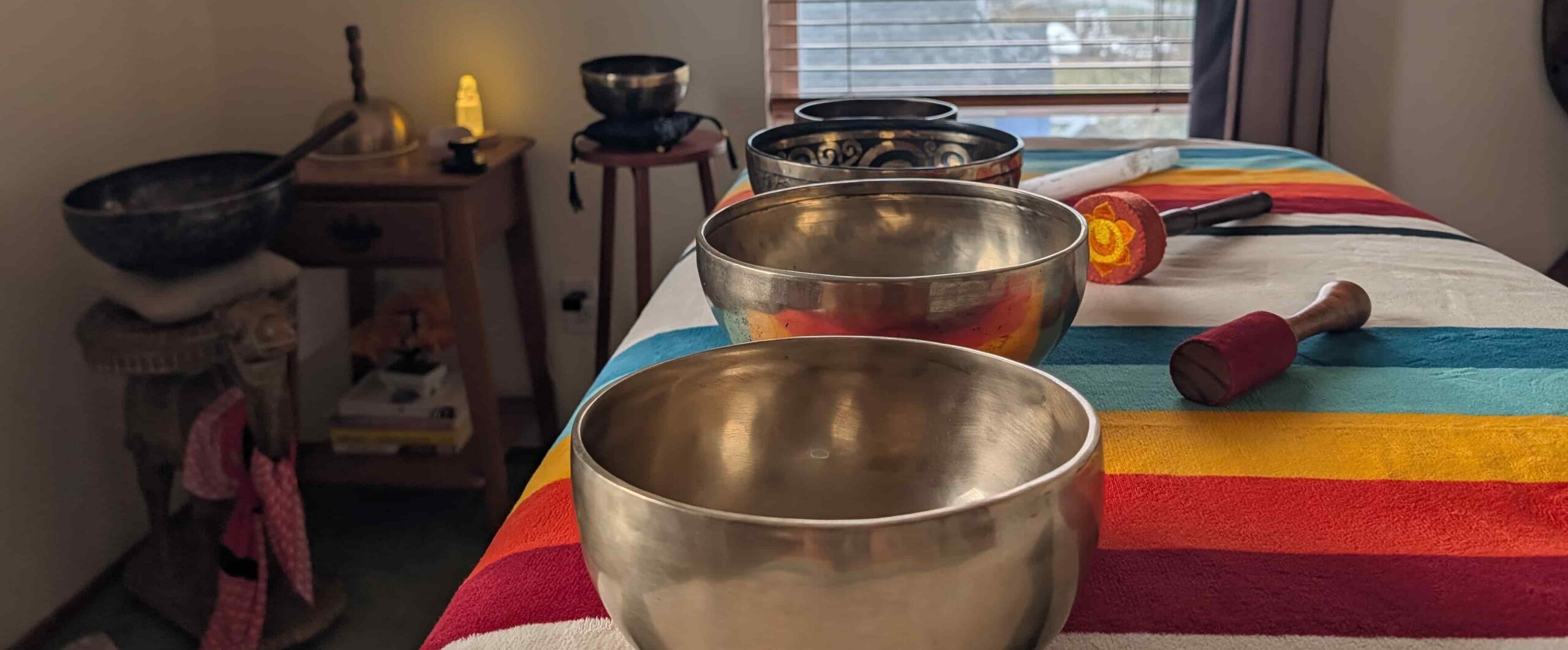 Tibetan singing bowls, mallets, and a selenite wand arranged on a treatment table for a private sound healing session in Anacortes