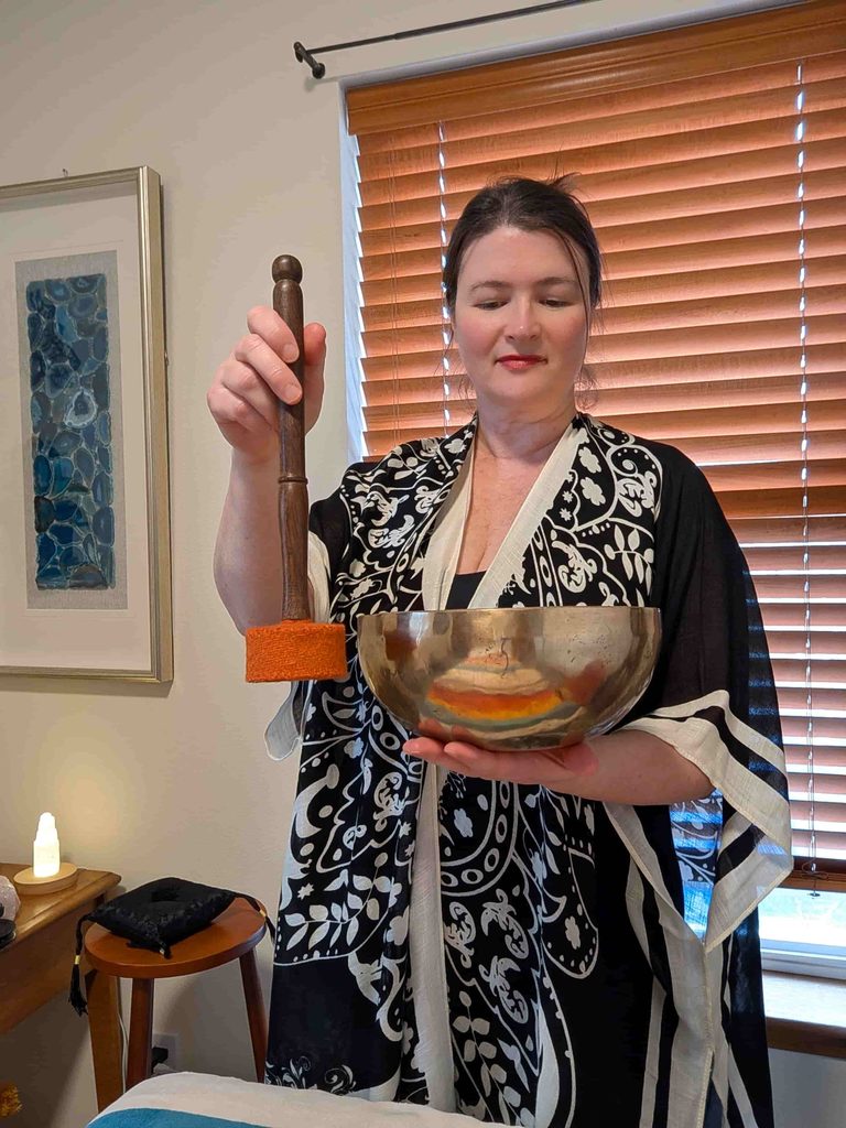 Sound healing practitioner Lara Dunning holding a Tibetan singing bowl and mallet in her Anacortes healing room